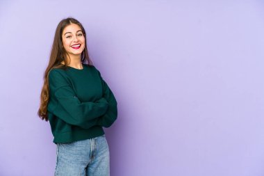 Mor arka planda izole edilmiş genç beyaz bir kadın. Kendine güveniyor, kararlılıkla kollarını kavuşturuyor..