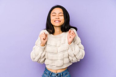 Mor bir arka planda izole edilmiş genç Çinli kadın mutlu ve başarılı hissediyor. Zafer konsepti.