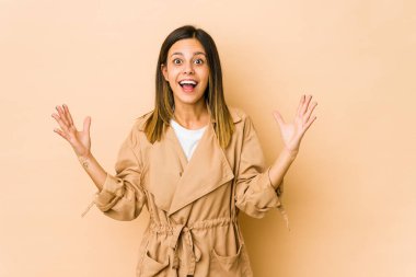 Bej arka planda izole edilmiş genç bir kadın hoş bir sürpriz alıyor, heyecanlı ve el kaldırıyor..