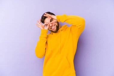 Mor arka planda izole edilmiş genç beyaz adam gözlerinde sorun olmadığını gösteriyor.