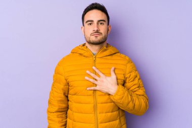 Mor arka planda izole edilmiş genç beyaz adam yemin ediyor, elini göğsüne koyuyor..