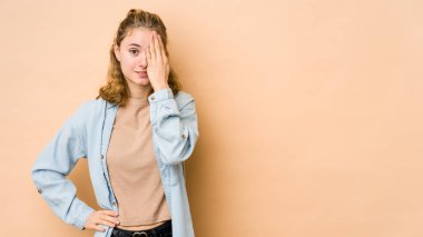 Beyaz tenli, bej arka planda izole edilmiş genç bir kadın yüzünün yarısını palmiye ile örterek eğleniyor..