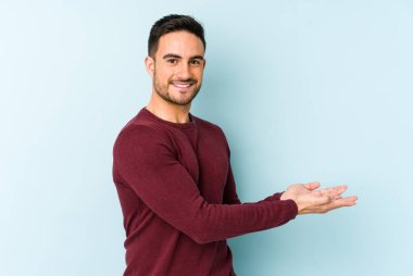 Mavi arka planda izole edilmiş genç beyaz bir adam palmiyesinde bir kopya alanı tutuyor..