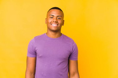 Sarı arka planda yalnız yaşayan genç Latin adam mutlu, güler yüzlü ve neşeli..