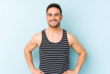 Kafkasyalı genç, mavi arka planda izole edilmiş. Kendine güvenen, kalçaları tutan biri..