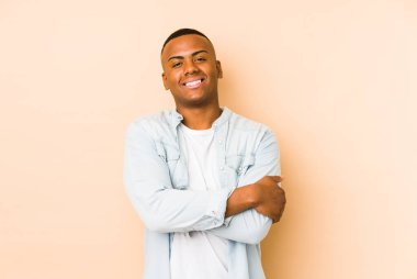 Bej arka planda izole olmuş genç Latin bir adam. Kendine güveniyor, kararlılıkla kollarını kavuşturuyor..