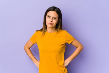 Mor arka planda izole edilmiş, hoşnutsuzca kaşlarını çatmış, kollarını kavuşturmuş genç bir kadın..