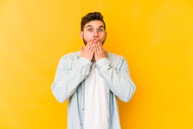 Sarı arka planda izole edilmiş genç beyaz adam elleriyle ağzını kapatırken şok oldu..