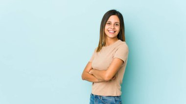 Mavi arka planda izole edilmiş, kendinden emin, kararlılıkla kollarını kavuşturan genç bir kadın..