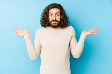 Genç, uzun saçlı, mavi bir arka planda izole edilmiş kafası karışmış ve omuz silken bir fotokopi alanını tutmak için şüpheli omuzlar..