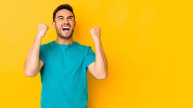 Sarı fırında izole edilmiş genç beyaz adam zaferden sonra yumruğunu kaldırıyor, kazanan kavram..