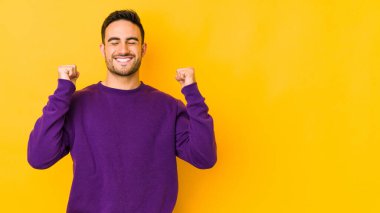 Sarı fırında izole edilmiş genç beyaz bir adam zaferi, tutkuyu ve coşkuyu kutluyor, mutlu bir ifade..