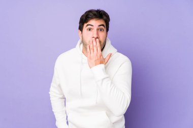 Mor arka planda izole edilmiş genç adam şok olmuş, ağzı ellerle kaplanmış, yeni bir şey keşfetmeye hevesli..