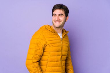 Mor arka planda izole edilmiş genç adam gülümseyen, neşeli ve keyifli bir kenara bak..
