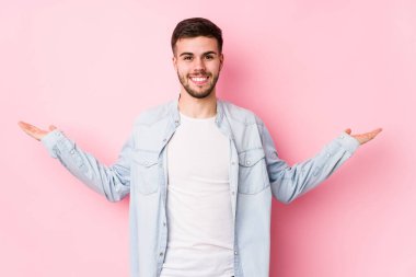 Beyaz arka planda poz veren beyaz tenli genç bir iş adamı kollarıyla ölçek yapar, mutlu ve kendinden emin hisseder..