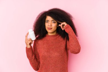 Vitaminlerini tutan genç afro kadın elinde vitaminlerle gezen genç afro kadın işaret parmağıyla hayal kırıklığı jesti yapıyor..