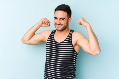 Mavi arka planda izole genç beyaz adam özel bir günü kutluyor, atlıyor ve enerjiyle kollarını kaldırıyor..