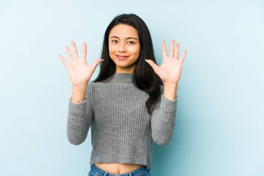 Mavi arka planda izole edilmiş genç Çinli kadın on numarayı elleriyle gösteriyor..