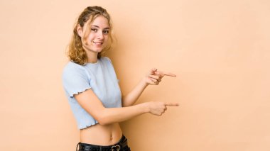 Beyazlı genç bir kadın bej arka planda izole edilmiş. İşaret parmaklarıyla işaret ettiği için heyecanlı..