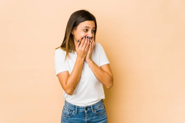 Bej arka planda izole edilmiş genç bir kadın bir şeye gülüyor, elleriyle ağzını kapatıyor..