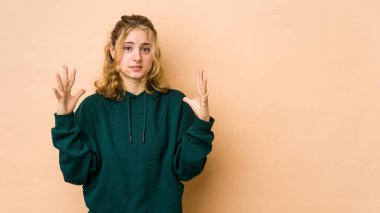 Beyaz tenli genç kadın bej arka planda izole edilmiş gökyüzüne haykırıyor, yukarı bakıyor, hayal kırıklığına uğramış..