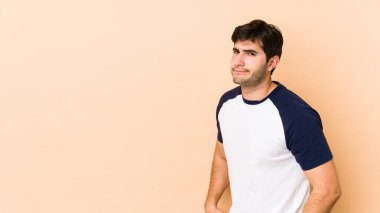 Bej arka planda izole genç adam hoşnutsuzca kaşlarını çatıyor, kollarını kavuşturuyor..