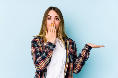 Mavi arka planda izole edilmiş genç beyaz kadın, avuç içinin fotokopi alanını tutmaktan etkilenmiş..