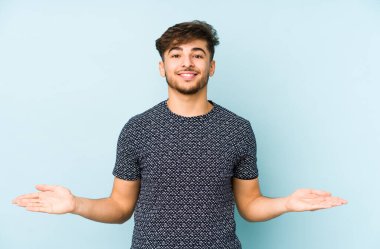 Mavi arka planda izole edilmiş genç bir Arap hoş bir yüz ifadesi sergiliyor..