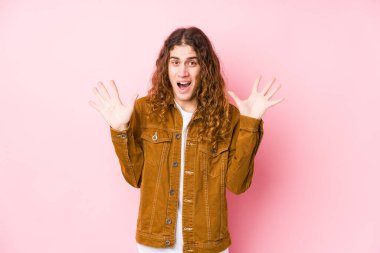 Genç, uzun saçlı adam zaferi ya da başarıyı kutlarken yalnız poz veriyor. Şaşırmış ve şok olmuş..