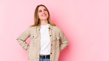 Genç beyaz kadın pembe arka planda izole edilmiş rahat ve mutlu bir şekilde gülüyor, boynunda dişlerini gösteriyor..