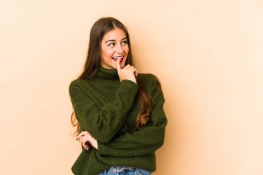 Beyaz tenli genç bir kadın, bej arka planda izole edilmiş, rahat bir şekilde bir şeyin fotokopi odasına baktığını düşünüyor..