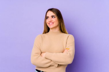 Mor arka planda izole edilmiş genç beyaz kadın kollarını kavuşturarak gülümsüyor..
