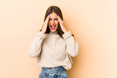 Beyaz tenli genç bir kadın bej arka planda izole edilmiş. Yüzünün yarısını palmiye ile kaplayarak eğleniyor..