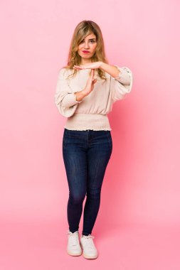 Pembe arka planda duran genç, sarışın, beyaz bir kadın bir jest yapıyor..