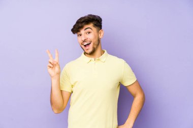 Mor arka planda izole edilmiş genç bir Arap adam neşeli ve kaygısız parmakları olan bir barış sembolü gösteriyor..