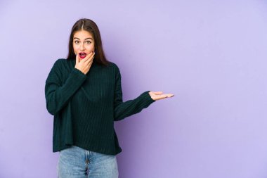 Mor arka planda izole edilmiş genç beyaz kadın avuç içinde fotokopi alanı tutuyor, el üstünde tutuyor. Şaşırmış ve mutlu..