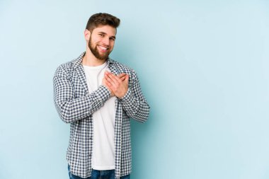 Mavi arka planda izole edilmiş beyaz bir genç, dost bir ifadeye sahip, avuçlarını göğsüne bastırıyor. Aşk konsepti.