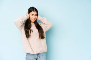 Mavi arka planda izole edilmiş genç bir Hintli kadın kulaklarını elleriyle kapatıyor..