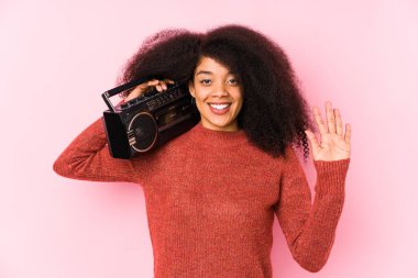 Elinde kaset tutan genç bir afro kadın. Beş numarayı parmaklarıyla mutlu bir şekilde gösteriyor..