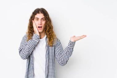 Uzun saçlı, yalnız poz veren genç bir adam avucunun içinde fotokopi alanı tutuyor, el üstünde tutuyor. Şaşırmış ve mutlu..