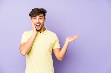 Mor bir arka planda izole edilmiş genç bir Arap, avuç içinde fotokopi alanı tutuyor, el üstünde tutuyor. Şaşırmış ve mutlu..