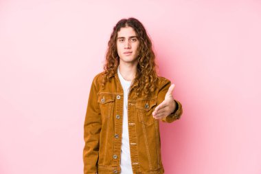 Genç, uzun saçlı adam kameraya el sallayarak selam veriyor..