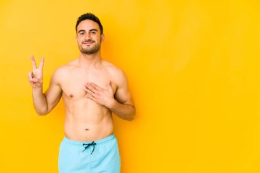 Sarı arka planda mayosu olan genç beyaz bir adam. Yeminli beyaz bir genç, elini göğsüne koyuyor..