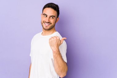 Mor arka plan noktalarında izole genç beyaz adam başparmak uzakta, gülüyor ve kaygısız.