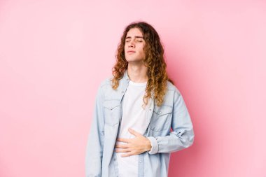 Uzun saçlı yalnız poz veren adam karnına dokunur, nazikçe gülümser, yemek yer ve tatmin olur..