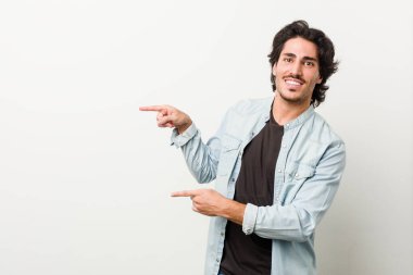 Beyaz bir arka planı olan genç yakışıklı adam işaret parmaklarıyla işaret ederek heyecanlanıyor..