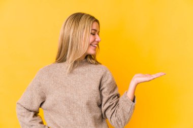 Sarışın, beyaz bir kadın. Sarı arka planda izole edilmiş. Bir avuç içinde fotokopi alanı var..