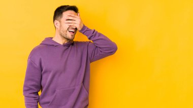 Sarı fırında izole edilmiş genç beyaz adam elleriyle gözlerini kapatıyor, geniş bir gülümsemeyle bir sürpriz bekliyor..