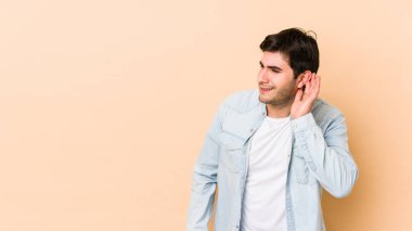 Bej arka planda izole edilmiş genç bir adam bir dedikoduyu dinlemeye çalışıyor..