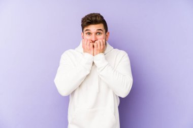 Mor arka planda izole edilmiş, tırnak yiyen, gergin ve endişeli genç bir beyaz adam..